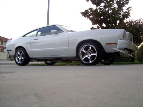 1978 Ford Mustang II - A white coupe with a distinctive fastback profile and aftermarket wheels is parked on a concrete surface.