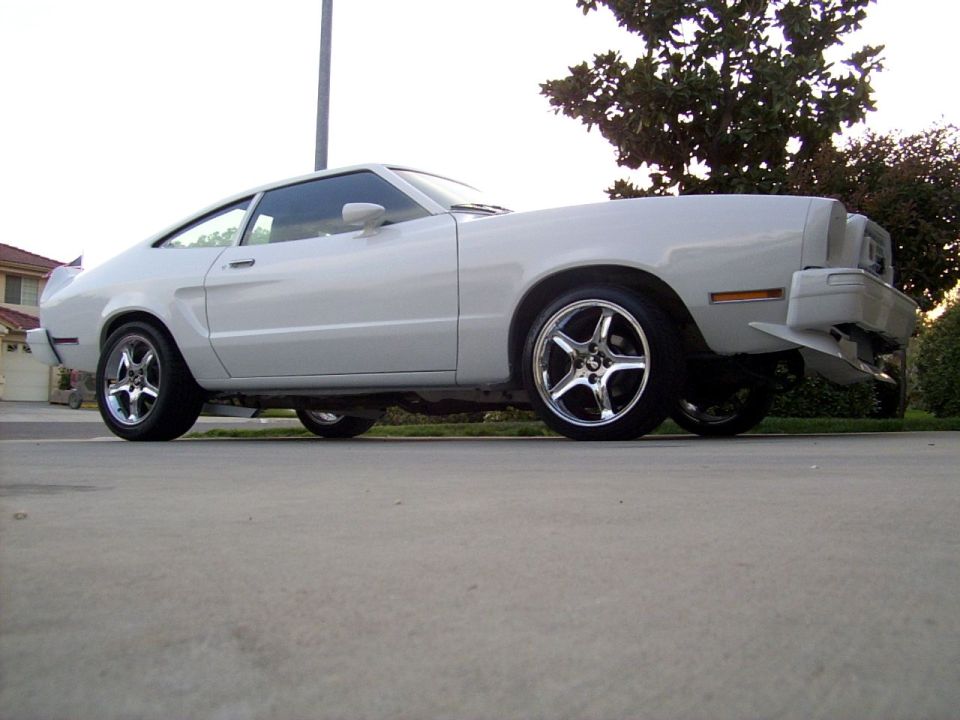 White coupe car with aftermarket wheels, seen from the side at a low angle