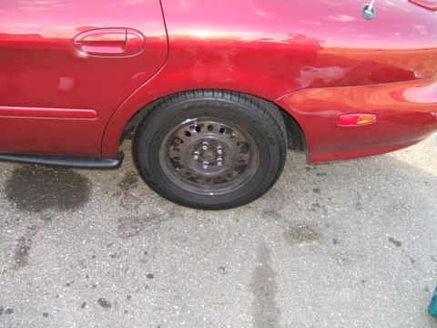 1998 Ford Taurus - Rear quarter panel and wheel of a red 1998 Ford Taurus, viewed from the side.