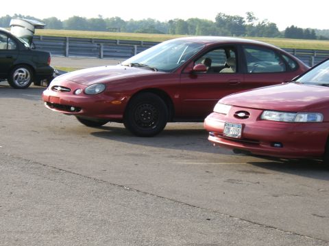 1998 Ford Taurus - Two red sedans are parked on asphalt, possibly at a race track.