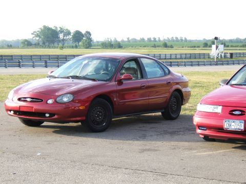 1998 Ford Taurus - A red 1998 Ford Taurus is parked on a track with another vehicle nearby.