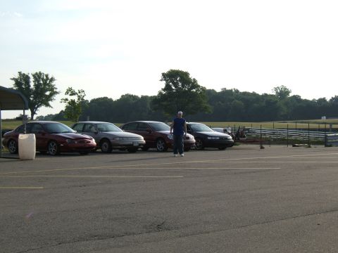 1998 Ford Taurus - Several sedans are parked in a lot next to a track, with a person standing between them.