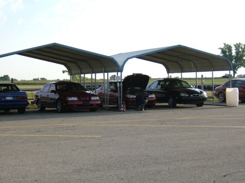 1998 Ford Taurus - Several cars are parked under a covered shelter, with one vehicle's hood open as someone works on the engine.