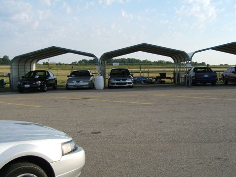 1998 Ford Taurus - Several cars are parked under metal carports on a paved lot under a partly cloudy sky.