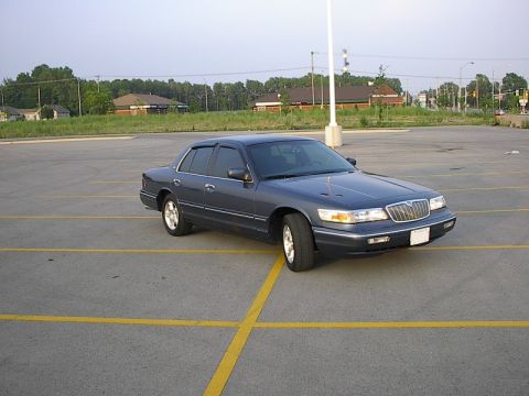 1985 Mercury Grand Marquis - A dark blue Mercury Grand Marquis is parked in a paved lot with yellow lines.