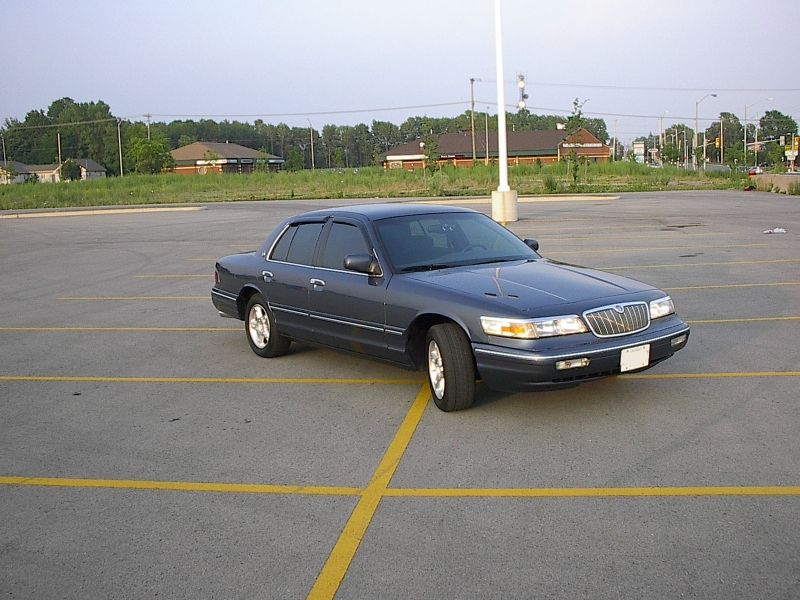 Blue-gray Mercury sedan in an empty parking lot at dusk, front three-quarter view