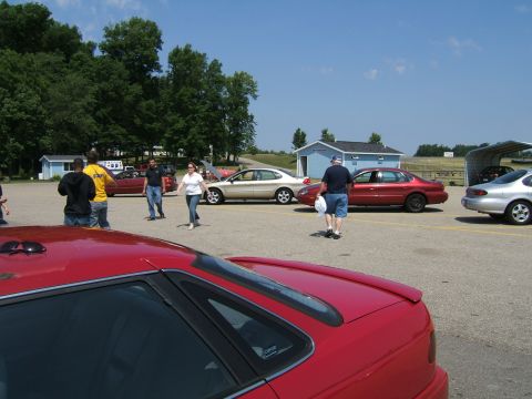 1998 Ford Taurus - People gather around cars in an outdoor lot on a sunny day.