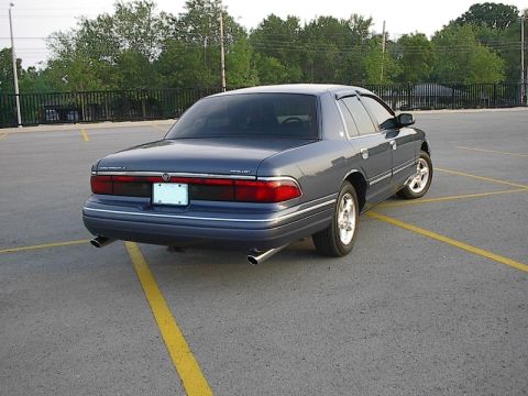 1985 Mercury Grand Marquis - The rear of a blue Mercury Grand Marquis is shown parked in a lot with yellow lines.