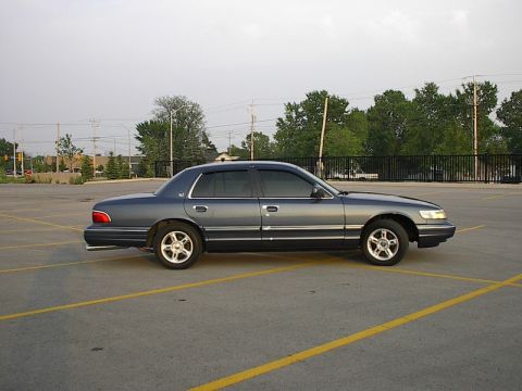 1985 Mercury Grand Marquis - Side view of a dark blue 1996 Mercury Grand Marquis sedan parked in a lot.