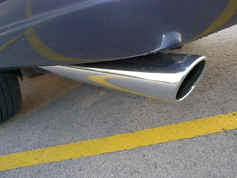1985 Mercury Grand Marquis - Close-up of a shiny exhaust pipe on a vehicle, with yellow lines visible on the ground.