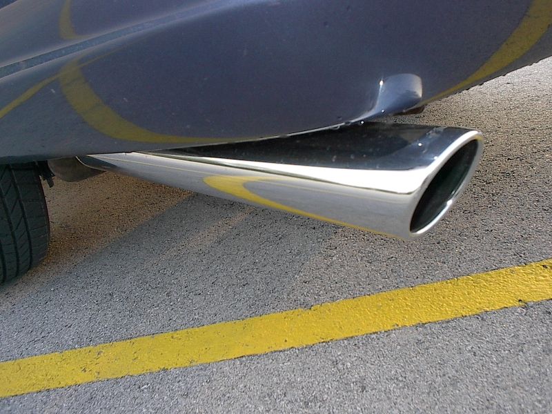 Chrome angle-cut exhaust tip under the rear bumper of a blue-grey car on striped asphalt