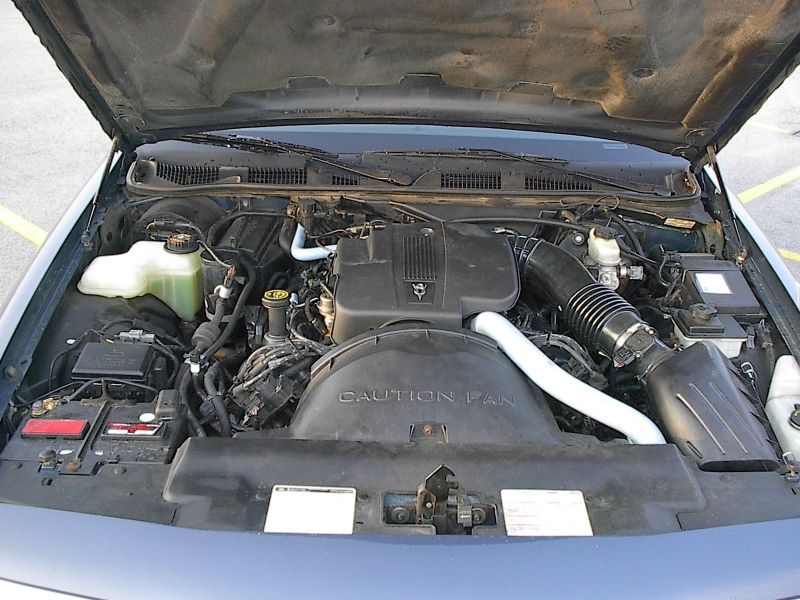 V8 engine bay of light blue sedan with CAUTION FAN shroud and airbox