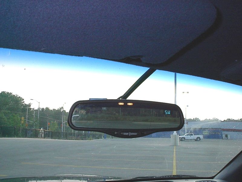 Interior rearview mirror with compass display showing SW, parking lot beyond windshield