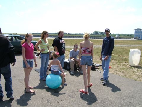 1998 Ford Taurus - A group of people are gathered around a green sedan on a sunny day.