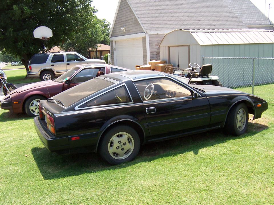 Black Z31 Nissan 300ZX on grass, rear three-quarter view, with a maroon 300ZX behind it