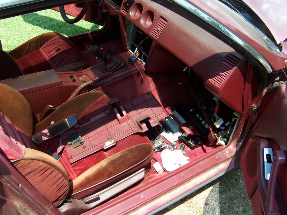 Disassembled burgundy interior of an 80s sports coupe with seat removed and wiring exposed