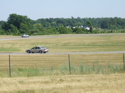 1998 Ford Taurus - Two sedans drive on a racetrack under a clear sky, with trees and buildings in the background.
