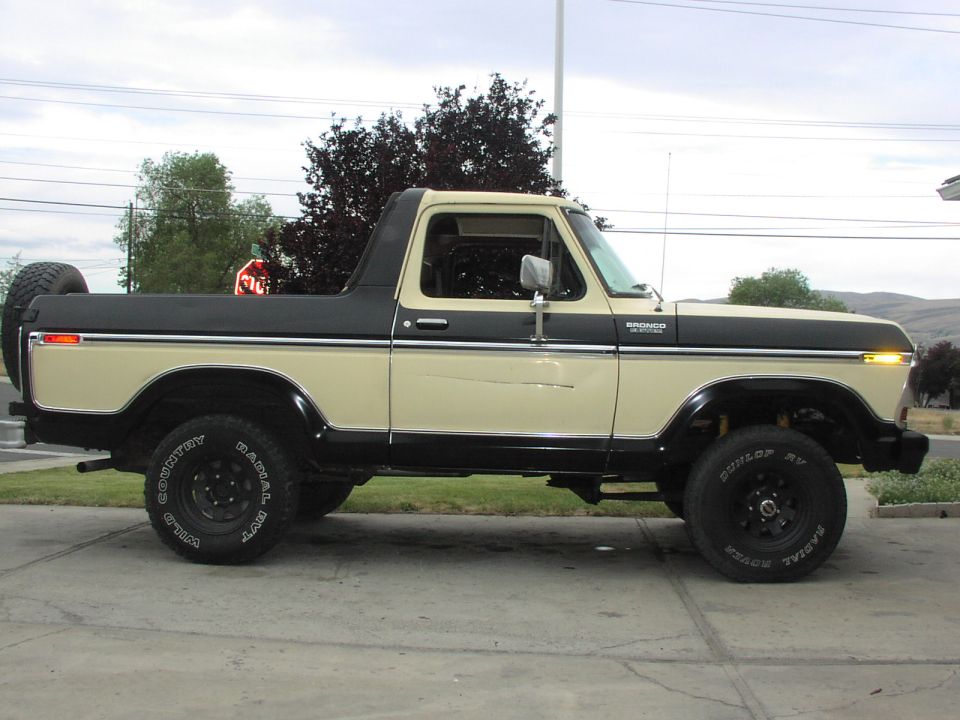 Tan and black lifted vintage Ford Bronco with soft top down, side profile
