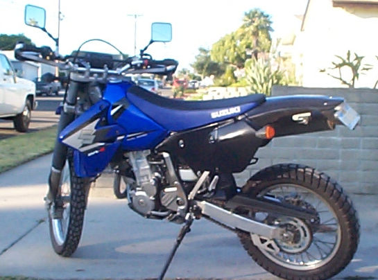 Blue and black Suzuki DR-Z400S motorcycle parked on a sidewalk, 3/4 front view