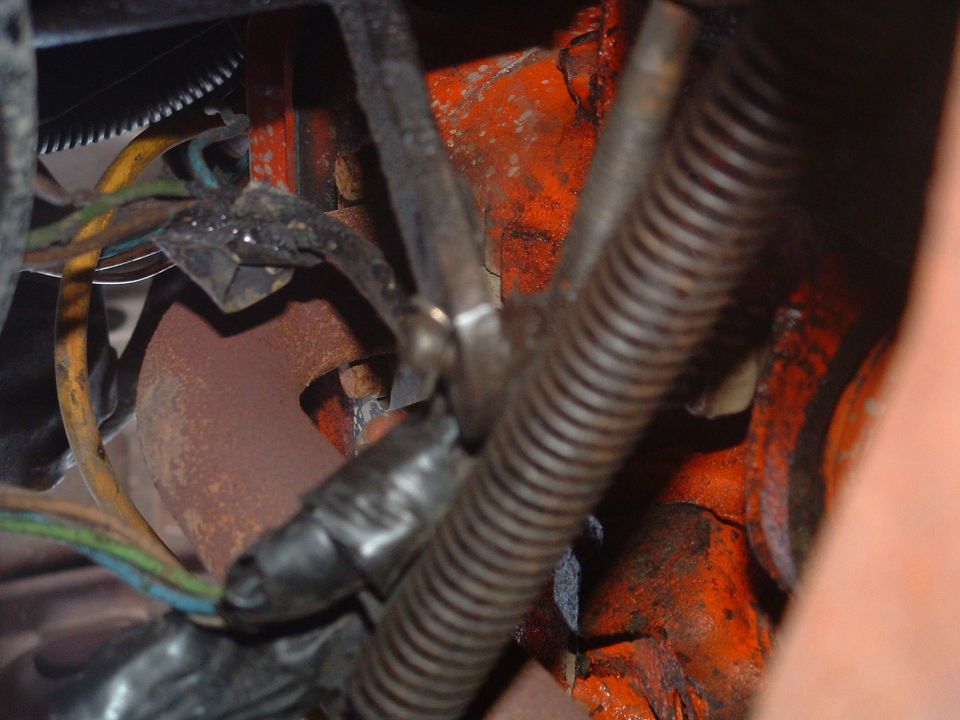 Close-up of corroded engine bay area with wiring loom, ribbed hose and bolt on orange-painted casting