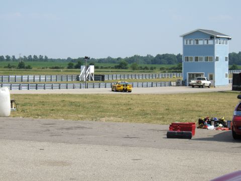 1998 Ford Taurus - A yellow sports car is on a racetrack near a blue building and a white pickup truck.