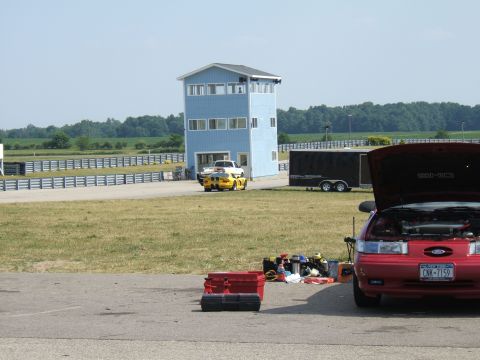 1998 Ford Taurus - A red sedan sits with its hood open at a racetrack, with a blue building and trailer nearby.