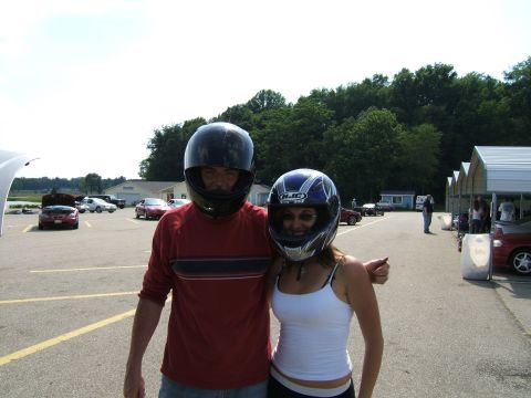 1998 Ford Taurus - Two individuals in racing helmets pose for a photo at what appears to be a track day event, with several cars visible in the background.