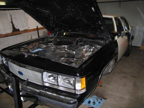 1991 Ford LTD Crown Victoria - The engine bay of a 1991 Ford Crown Victoria is exposed for maintenance in a garage setting.