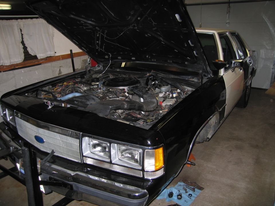 Front view of a 1991 Ford Crown Victoria with hood open showing the engine bay. The car is in a garage
