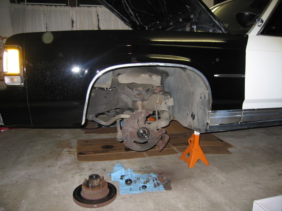 Front brake and hub work on a black car raised on an orange jack stand in a garage
