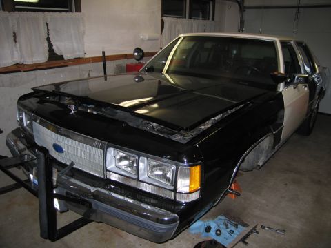 1991 Ford LTD Crown Victoria - This Ford Crown Victoria police car is undergoing maintenance in a garage, with its hood up and front wheels removed.