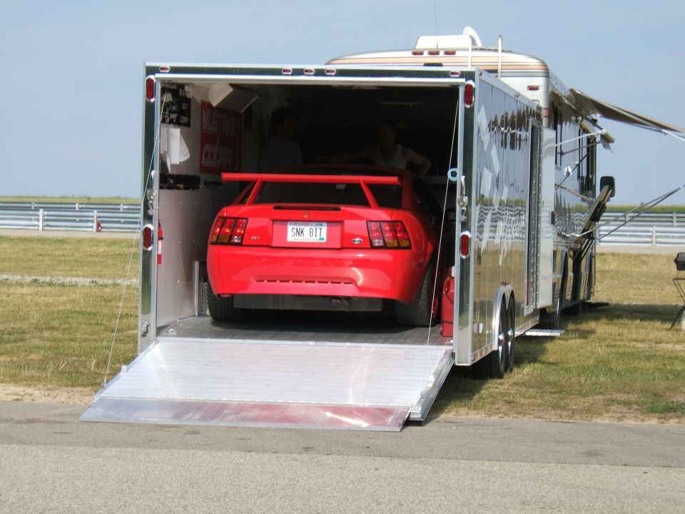 Red Ford Mustang with a spoiler being loaded into a trailer