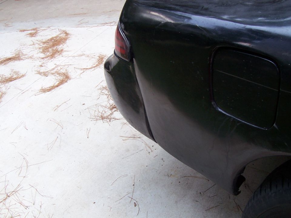 Dented dark green rear quarter and bumper cover with fuel door on a concrete pad