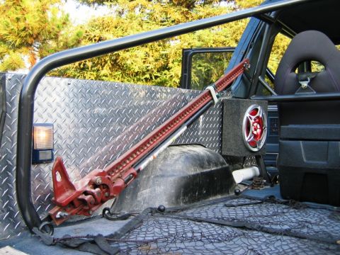 1985 Ford Bronco - A red hi-lift jack is secured in the cargo area of a vehicle, alongside a speaker and netting.