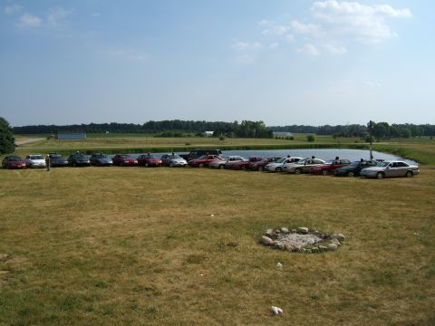 1998 Ford Taurus - A collection of sedans and SUVs are parked in a grassy field near a body of water under a clear sky.