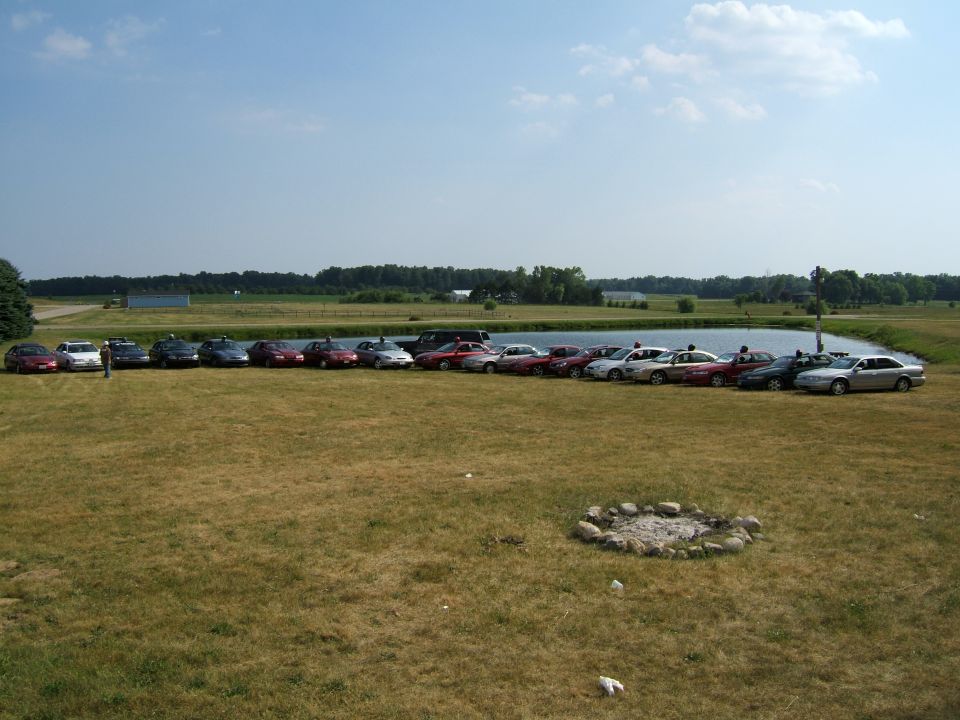 many cars parked in a row next to a pond on a sunny day