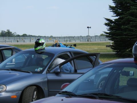 1998 Ford Taurus - A gray 1998 Ford Taurus sits with its door open, a green helmet resting on its roof, at what appears to be a race track.