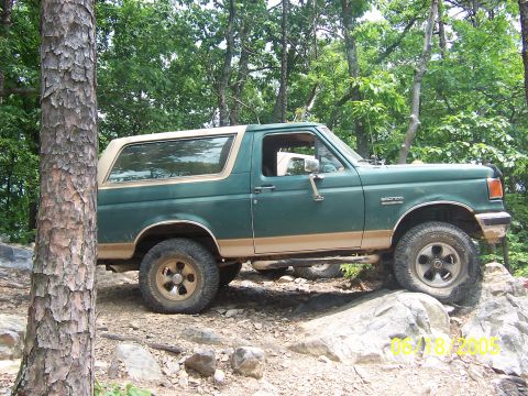 1978 Ford Bronco - A green Ford Bronco with tan trim navigates a rocky trail.