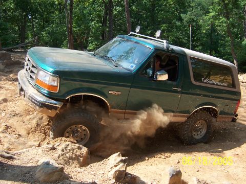 1978 Ford Bronco - Green Ford Bronco off-roading on a dirt trail, kicking up dust.