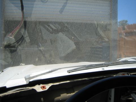 1990 Ford Bronco - Interior view through a dusty windshield over the cowl and wiper, with a steering wheel and wiring visible inside.