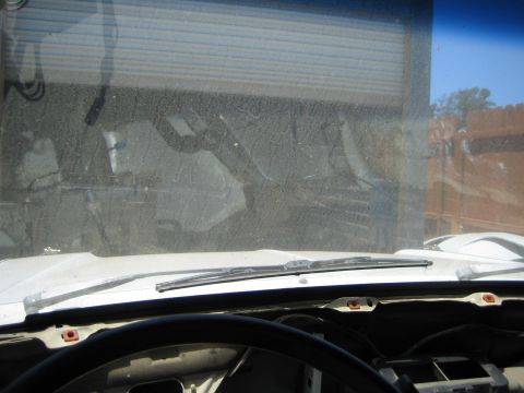 1990 Ford Bronco - View through a grimy windshield from the driver area showing the cowl, wiper arm and a building seen outside.