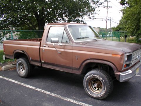 1979 Ford Bronco - This brown pickup truck is parked in a lot with trees in the background.