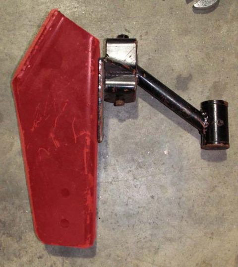 1988 Ford Bronco - This is a red metal bracket with a black arm, likely a vehicle part, shown against a concrete background.