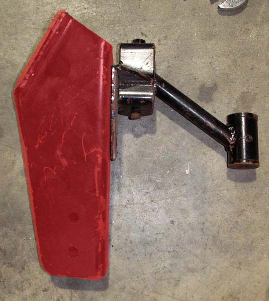 Red metal bracket attached to a black metal arm, resting on a concrete surface