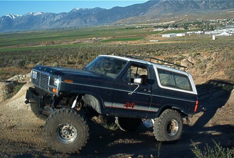 1986 Ford Bronco - Modified 1986 Ford Bronco climbing a dirt incline with mountains in the background.