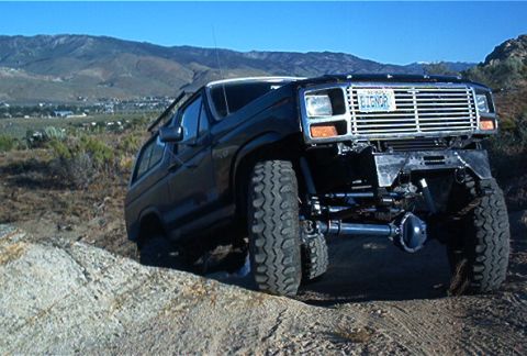 1986 Ford Bronco - This modified Ford Bronco is tackling an off-road trail with a mountainous landscape in the background.