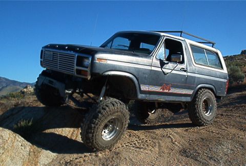 1986 Ford Bronco - This modified Ford Bronco navigates a rocky, off-road terrain under a clear blue sky.