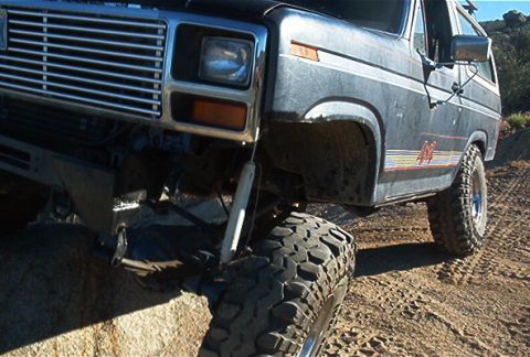 1986 Ford Bronco - This 1980s Ford Bronco is shown in a three-quarter front view, equipped with off-road tires and navigating a dirt trail.