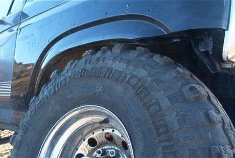 1986 Ford Bronco - Close-up of a dark blue Ford Bronco's fender and large off-road tire.