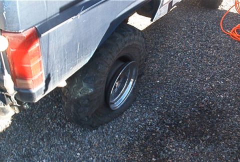 1986 Ford Bronco - A vehicle has a flat tire, with the rear section of the body and wheel clearly visible.